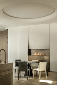 Modern dining room featuring a circular metallic table with white cushioned chairs and a minimalist fireplace.