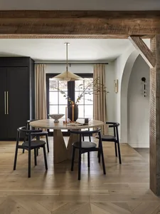 A modern dining room featuring wooden beams, a round table, and black chairs.