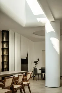 A modern dining room with white concrete walls, wooden furniture, and a large skylight.