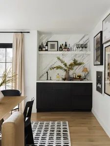 Modern kitchen with black cabinets, marble backsplash, and hardwood floors.