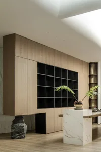 A modern living room and library featuring wooden shelving, leather seating, marble tables, metal accents, and potted plants.