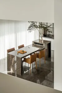 A sleek, modern kitchen dining space featuring marble countertops, brown leather chairs, and a large window allowing natural 