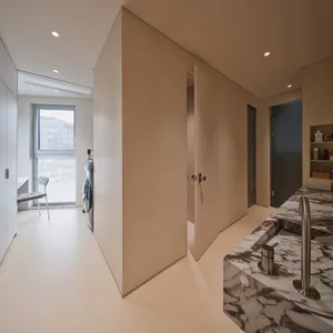 A minimalist modern laundry room featuring marble countertops and white cabinets.