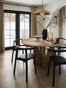 A modern minimalist dining room with a wooden table, black chairs, and a large pendant light.
