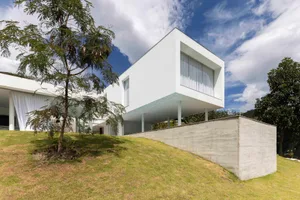 A modern, minimalist home with a white, concrete exterior featuring large glass windows and a cantilevered structure.