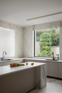 Modern, minimalist kitchen featuring marble countertops and backsplash, with a large window offering a view of lush greenery.