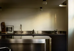 A modern minimalist kitchen with metallic finishes, featuring a sleek countertop and stainless-steel appliances.
