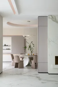 A minimalist dining room featuring a round marble table with a modern light fixture and beige upholstered chairs. Decorative 