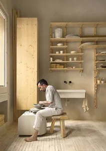 A minimalist pottery studio featuring wooden shelves and a bench, with a man working on a potter's wheel.
