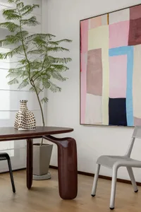 A minimalist living room with a wooden table, ceramic vase, and abstract painting.