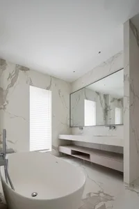 A modern bathroom with marble walls, a large mirror, and a freestanding tub.