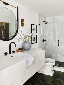 Modern bathroom with marble walls and floor, white sink, and black fixtures.