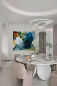 A modern dining room featuring a round marble table, fabric chairs, and abstract art.