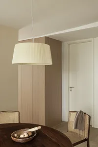 A modern dining room with a wooden table, chairs with woven backs, and a pleated pendant light hanging above.