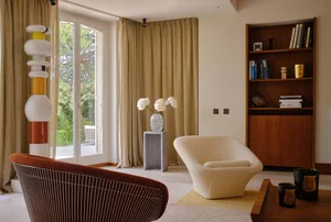 Modern living room featuring textured fabrics and wood furniture, with a bookshelf, white flowers, and a unique geometric cha