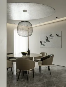 A modern minimalist dining room with a round marble table, upholstered leather chairs, and a black wireframe pendant light ha