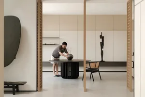 A man arranging a vase on a round table in a minimalist residential interior with concrete, wood, and metal materials.