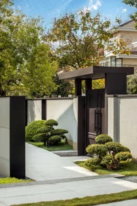 Concrete and metal entrance with small bonsai trees and greenery surrounding it.