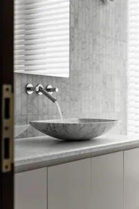 A minimalist bathroom with a marble countertop featuring a sleek, modern sink and faucet.