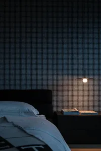 A minimalist bedroom featuring a checkered fabric wall, a black bed with a white blanket, and a hanging pendant light on a be
