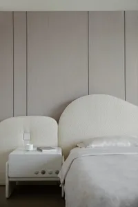Minimalist bedroom featuring a bed with beige textured fabric headboard and bed frame, against a textured beige wall, with a