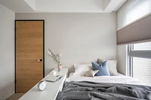 A minimalist bedroom with neutral-toned walls, bedding, and window treatments, featuring a modern wooden door and a sleek whi