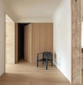 Modern minimalist interior with oak wood flooring, walls, and wardrobe, featuring a black chair.