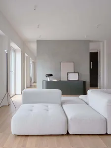 Modern minimalist living room with light gray fabric furniture, wooden floor, and minimalistic decor.
