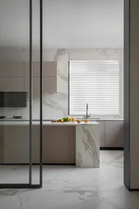 A minimalist residential kitchen with marble countertops and floor, featuring a kitchen island and a window with blinds.