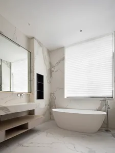 A modern bathroom featuring marble walls and floor, a freestanding bathtub, a floating vanity with a large mirror, and a wind