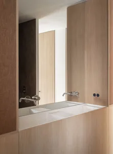 Modern minimalist bathroom with wooden fixtures and a long, rectangular sink with faucets.