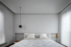 A minimalist modern bedroom with a light grey textured wall panel in the background and a white bed with floral bedding in th