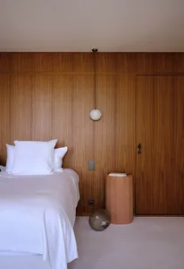 A modern bedroom featuring wood-paneled walls, minimalist design, and a white bed with a simple nightstand and spherical tabl