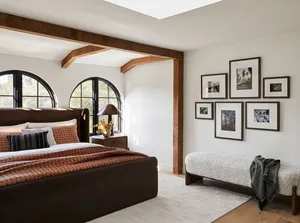 Modern bedroom showcasing a brown leather bed, wooden beams, and framed photographs on the wall.