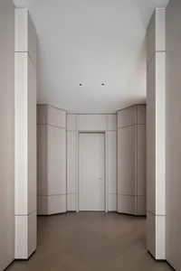 A modern corridor featuring grey-toned walls and flooring, with a closed door at the end.