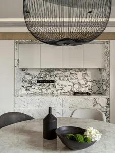 A modern kitchen featuring marble countertops and cabinets against a white marble backsplash, with a sleek vase and bowl of f