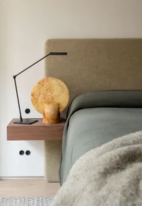A modern minimalist bedroom featuring a upholstered bed with a large headboard, a floating nightstand with a black lamp and m