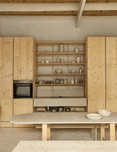 A modern, minimalist kitchen with wooden cabinetry, a concrete countertop, and open shelving.