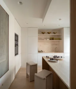 Modern minimalist kitchen with marble countertops, wooden stools, and sleek, white cabinetry.