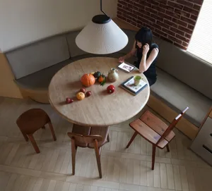 A minimalist dining area featuring a stone table surrounded by wooden chairs and a cushioned bench, with vegetables and a tab