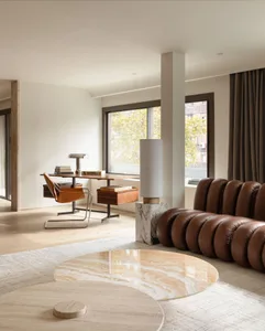 A minimalist living room with a round marble coffee table, brown leather sofa, and wooden desk.