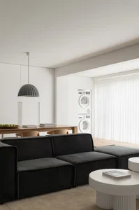 A modern living room featuring a black sofa on white flooring, with a wooden table in the background.