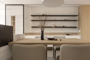 A modern dining room with white walls, wooden table, and minimalist shelves.