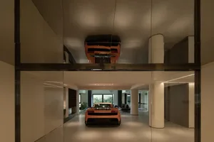 Modern garage with concrete walls and floor, featuring a luxury sports car and a second car parked above on a lift.