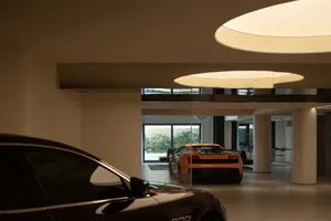 A modern garage with glass walls and floor, featuring high-end sports cars.