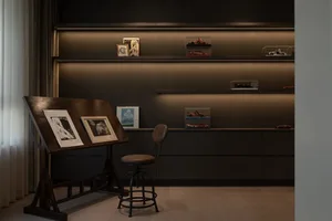 Modern home office with a wooden drafting table, framed artwork, and display shelves with model cars.
