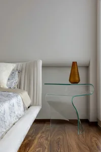 A modern bedroom interior featuring a glass nightstand with a unique curved shape.