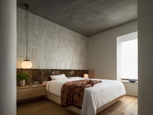 A modern minimalist bedroom with concrete walls and bed placed centrally with a patterned blanket and a small nightstand with