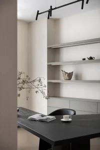 A modern minimalist office space with a black desk, wooden elements, and concrete shelving.