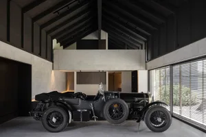 A vintage black car parked in a spacious garage with concrete walls and high ceilings.